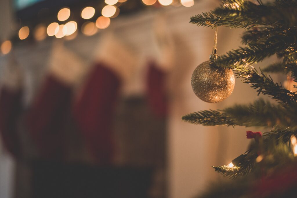Christmas tree in focus with an ornament dangling with stockings and Christmas lights blurred in the background