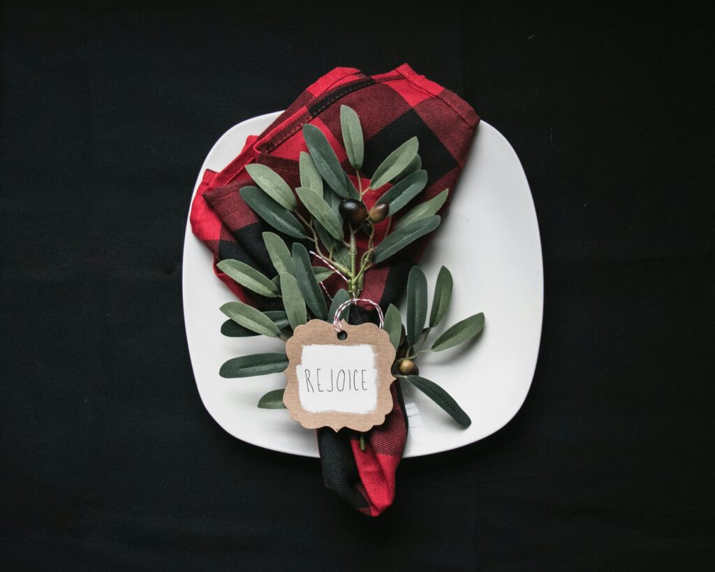 A plate with a red napkin and holiday leaves and berries with a note saying rejoice